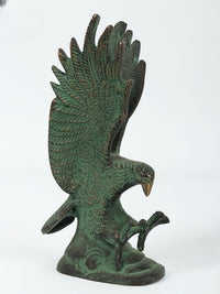 Green eagle sculpture standing with one wing lifted, ornate feather carvings on brass base