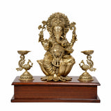 Brass seated Lord Ganesha on wooden base with two peacock lamp holders