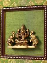 Brass Gajalakshmi idol framed, side attendants holding vessels, gold-toned detail