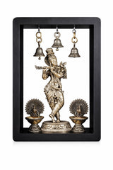 Brass Lord Krishna idol with three hanging bells and two oil lamps in a frame