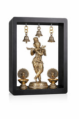 Standing brass Krishna idol with flute, three hanging bells, and two standing oil lamps