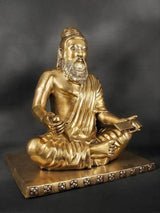 Brass Valmiki sculpture close-up: bearded face, layered robe folds, seated with book