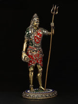Shiva brass idol side view, trident upright, red-and-green patterned outfit, 12 in