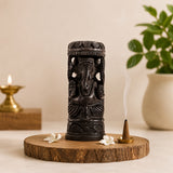 Dark carved Ganesha statue with crown, on round base with small incense and flowers