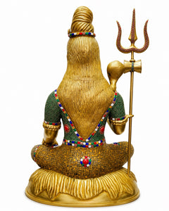 Seated brass Lord Shiva statue back view with long hair, green beaded outfit, raised trident