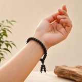 Black wooden bead bracelet on wrist with tassel ends and round bead strands