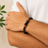 Black beaded bracelet on wrist with brown rudraksha-style beads and small damru charm