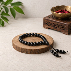 Kids' black beaded wood bracelet with small tassel ends, on wooden display.