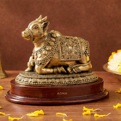 Brass Nandi bull idol seated on dark wooden base, ornate detailing