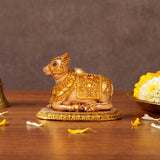 Seated golden resin Nandi bull statue with ornate saddle and detailed carvings on base