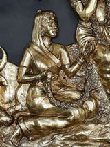 Brass Radha Krishna wall hanging close-up: Radha seated beside Krishna on the ground