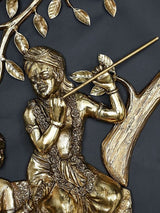 Brass Krishna figure with flute near tree trunk, ornate robes and swirling floral details