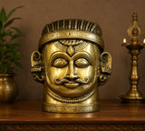 Brass Shiva mukha lingam idol front on tabletop, detailed eyes, hair, and mustache