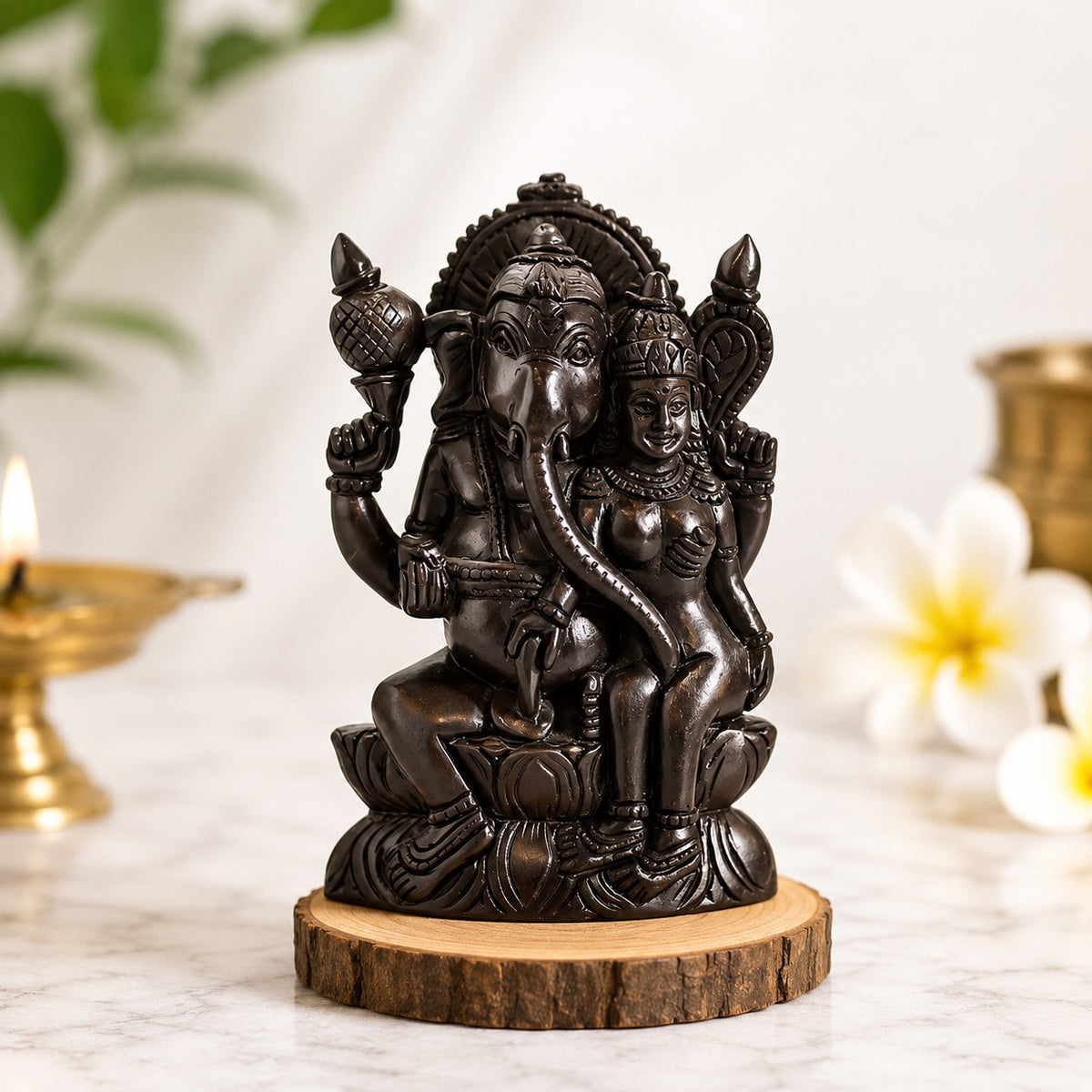 Dark metallic seated Ganapati statue on round wooden base with smaller attendant figure