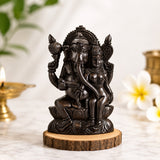 Dark metallic seated Ganapati statue on round wooden base with smaller attendant figure