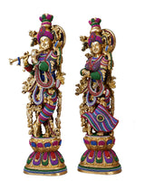 Brass Radha Krishna sculpture, one figure holding a flute, both with crowns and colorful robes.