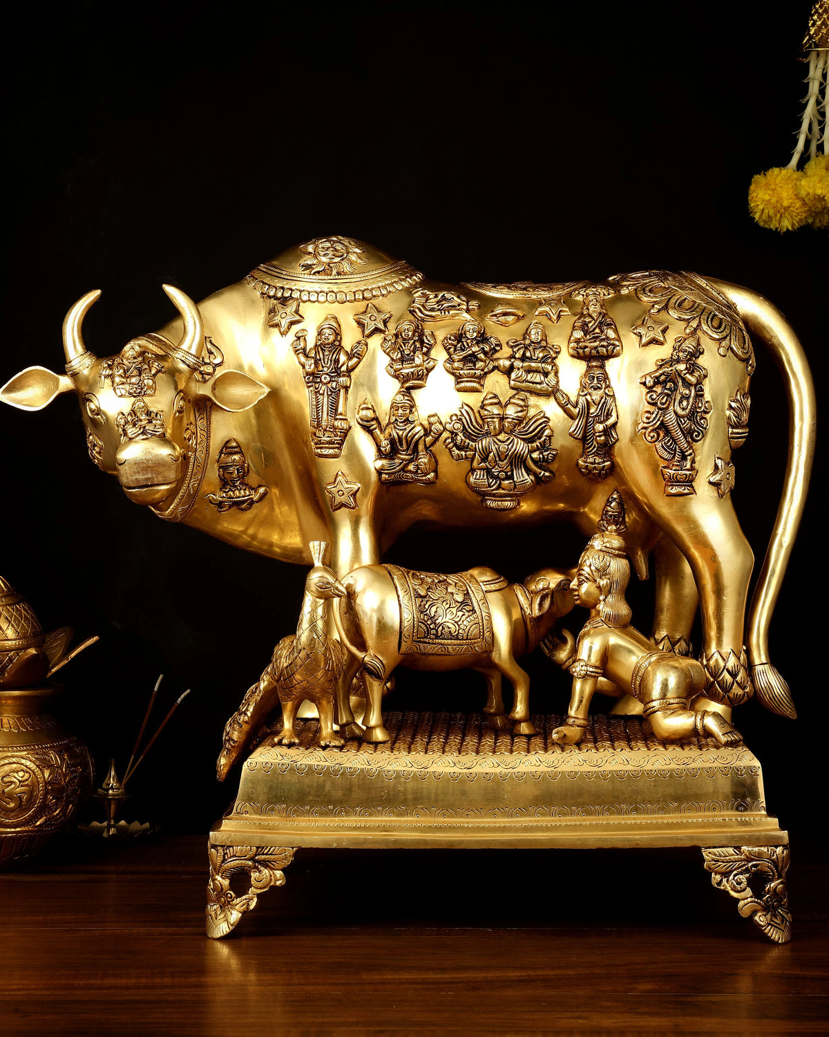 Brass Kamdhenu cow with calf statue, engraved deity figures, raised on ornate base