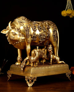Large brass cow and calf statue with detailed deity engravings and decorative pedestal