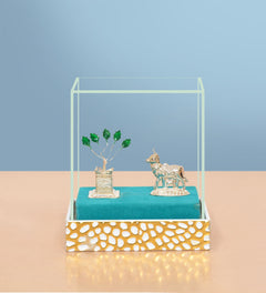 White metal Kamdhenu cow figurine beside tulsi plant in glass display box