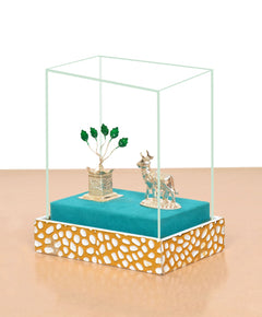 Top view of glass box showing white metal cow figurine and tulsi plant on blue base
