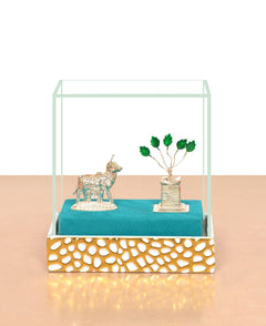 Tulsi plant centerpiece with white metal cow figurine on blue cloth in glass case
