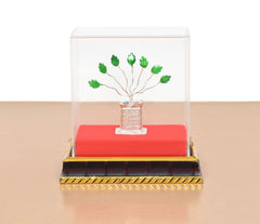 White metal Tulsi plant under clear dome, red base with silver pot and green leaves