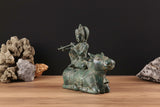 Bronze Krishna on cow statue, side view, holding a flute, ornate headdress