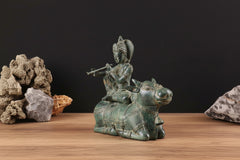Bronze Krishna on cow statue, side view, holding a flute, ornate headdress