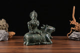 Bronze Krishna idol seated on cow, 3/4 angle, raised flute hand