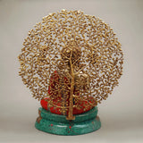 Back view of seated Buddha with tree trunk and branches, red robe, green base, gold-tone details