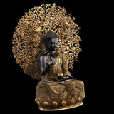 Buddha-Sitzstatue mit segnender Hand und goldverzierter Robe, umgeben von Baumdekor