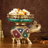 Gold brass elephant urli with green band, blue/red jeweled patches, and raised trunk