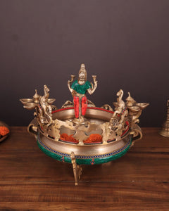Ashtalakshmi brass urli with diyas, deity figure standing above round tray with cups