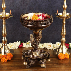 Brass urli centerpiece on ornate pedestal with chain rim holding flowers and side diyas