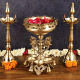 Brass urli with stand and two diya holders, ornate deity base, top bowl with red petals