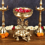 Gold-tone brass urli with stand and two diya holders; large bowl with red flower petals