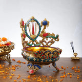Ornate brass urli bowl on four legs, chakra medallion with ribbon-like accents