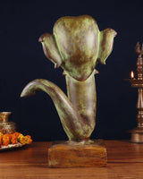 Brass Ganesha face showpiece, angled view with textured ears and trunk curl on base.