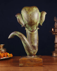 Brass Ganesha face showpiece, angled view with textured ears and trunk curl on base.