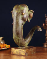 Ganesha face showpiece in brass with raised trunk curl, three-quarter view on base.