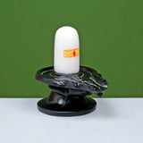 Front view of white lingam on ornate dark base with carved decorative details