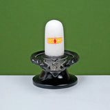 White shivling with orange-yellow emblem on black pedestal and circular base