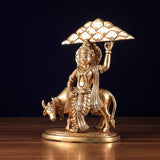 Brass Krishna idol under ornate Govardhan umbrella, holding arm raised beside bull