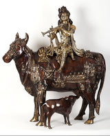 Krishna idol seated on cow figurine, dark brown and gold ornamented detailing