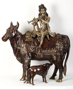 Krishna idol seated on cow figurine, dark brown and gold ornamented detailing