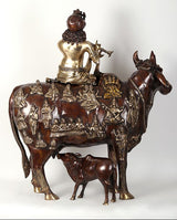 Krishna statue seated on cow, rear view with dark brown and gold ornamented panel