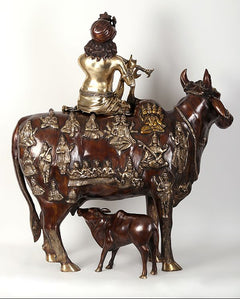 Krishna statue seated on cow, rear view with dark brown and gold ornamented panel