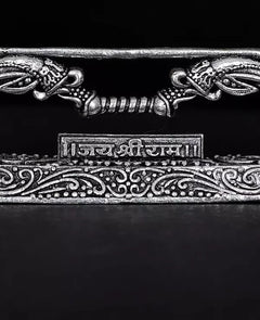 Brass Dhanushe close-up: curled motifs and central engraved Sanskrit panel