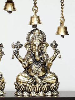 Close-up of seated Ganesha idol with ornaments and hanging bell chain overhead