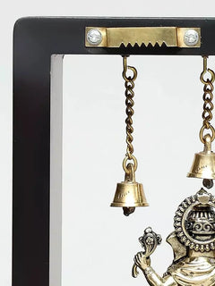 Hanging bells and chain on brass wall frame with part of Ganesha idol visible